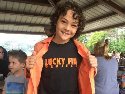 Hayden Rolence is wearing a red shirt and a tees with Lucky Fin Project written on it.